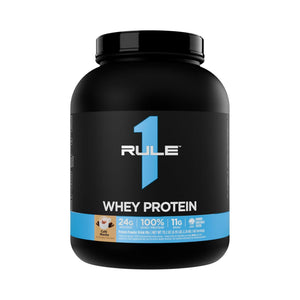 A black tub of RULE 1 Whey Protein powder, vanilla flavor, on a solid white background.