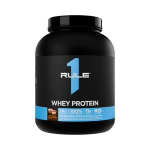 A black tub of Rule 1 Whey Protein powder, Chocolate Flavored, on a solid white background.